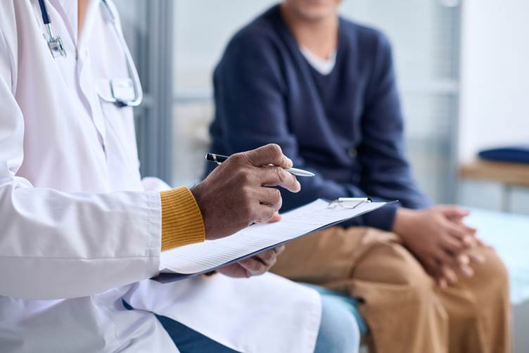 A picture of a doctor holding a clipboard giving a patient sat on a bed behind them a diagnosis 