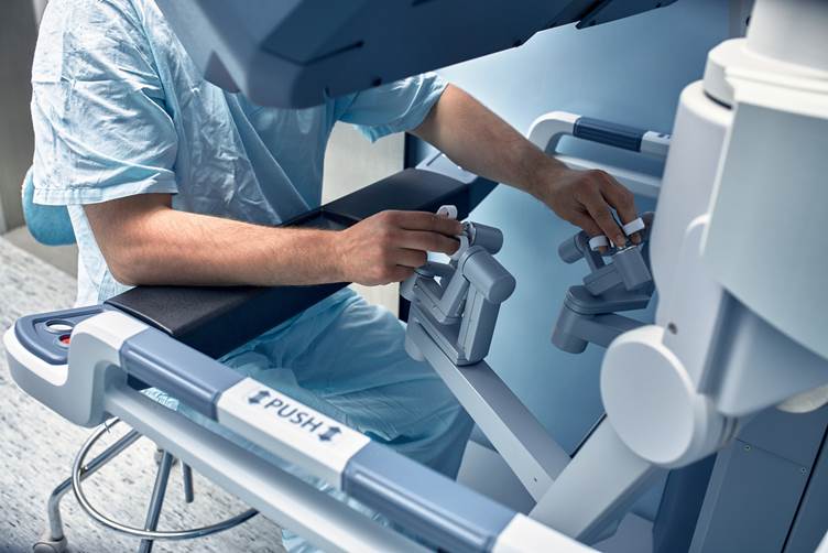 A surgeon sat at a robotic surgery machine using the controls to conduct surgery 